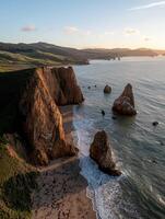 Waves crashing against dramatic cliffs and rock formations at sunset photo