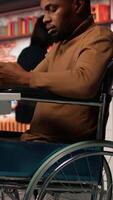 Vertical Engineer with disability coding AI algorithms in inclusive startup office using tablet, refining machine learning models. Man in wheelchair coding on device in Silicon Valley workplace, camera A video