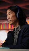 Vertical Senior admin coding advanced AI algorithm in startup office, refining machine learning models to enhance automation, wearing headphones. CTO manager listening music and coding, camera B video