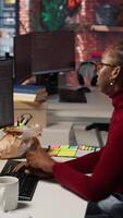 Vertical IT employee using programming languages on PC in AI startup office to build applications, enjoying snack. Woman using computer in artificial intelligence development agency, eating food, camera A video