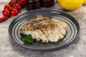 A piece of fish on a plate with lemon and tomatoes photo