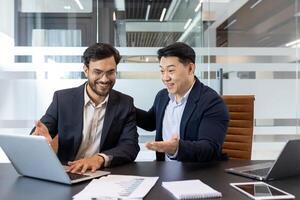 Male mentor at workplace helping intern learn new work project, two men in business suits working inside office at workplace. photo
