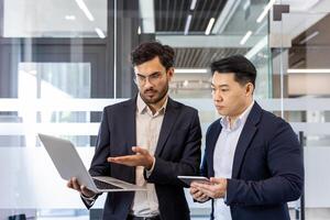 Business professionals engaged in discussion using laptop and tablet, emphasizing teamwork and technology. Office setting highlights collaborative work. Professionals analyze data, share insights photo