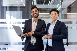Two confident professionals engage in business discussion using laptop and phone in modern office. Smiling colleagues demonstrate teamwork, collaboration, and effective communication photo