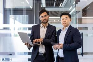 Two confident businessmen in modern office discussing project using technology. Professional atmosphere with focus on teamwork and collaboration. photo