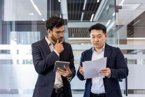Business professionals engaged in office setting, reviewing paperwork and discussing strategies. One holding digital tablet, indicating technology integration. Image captures teamwork photo