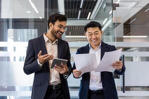 Two business professionals in office reviewing documents together with smiles. One holds a digital tablet, indicating technology use. They represent positive teamwork, professional collaboration photo