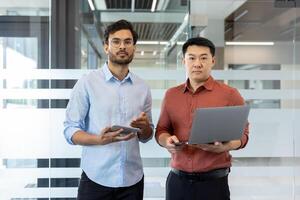 Two business professionals in a office environment interact using a laptop and a tablet. The image illustrates collaboration, teamwork, and the integration of technology photo