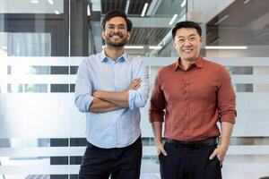 Portrait of two office colleagues in casual clothes. Men smiling and looking at camera, working inside office at workplace photo
