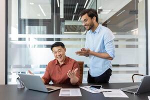 Two coworkers are seen in bright, modern office setting, energetically discussing and celebrating work success. The table displays graphs and a smartphone, emphasizing a productive workplace ambiance photo