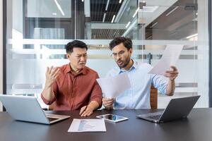 Two office workers checking financial reports and contracts, colleagues in casual clothes dissatisfied with the result, sad and unhappy, business people busy with paperwork photo