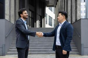 Two serious men in business suits greet each other shaking hands outside an office building. Diverse business people walking through the city. photo
