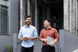 Two men walking and chatting outside an office building, colleagues and business partners taking a walk in the fresh air on their lunch break. photo