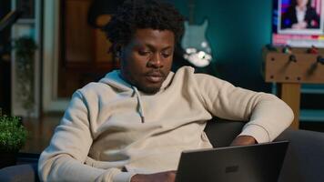 Black man does his research by reading articles and taking notes at home, collecting information for a new project. Freelancer multitasking and studying files with data driven papers. Camera A. video