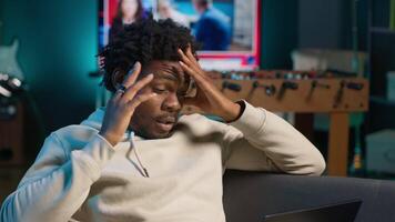 Black person having health problems suffering from headache and nausea, sitting in the living room and struggling to work on tasks. Remote worker suffering from illness at home. Camera A. video