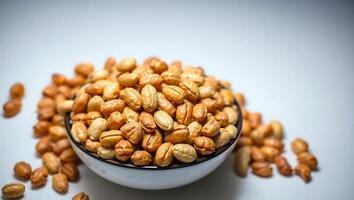 Roasted nuts in a bowl on a plain background with scattered pieces photo