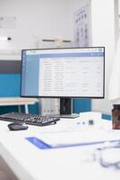 On desk of hospital office, desktop pc is displaying patient doctor appointments as documents, pill bottle, keyboard and mouse are placed nearby. Computer showing use of modern technology in a clinic. photo