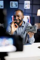 Media star excited to review newly launched V mount battery, comparing features with older models. Technology internet show host filming online channel, analyzing portable charging device photo