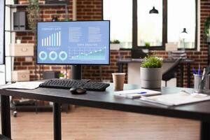 Organized workspace with computer monitor displaying data analysis, notebook, and documents on desk. Clean brick wall office with no people, ready for planning and project completion. photo