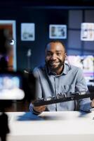 Cheerful BIPOC artist filming DJ mixing tutorial in recording studio, playing with samples and sound effects. Audio engineer showcasing music production equipment to audience photo