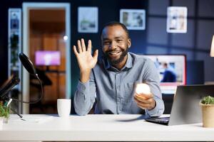 Influencer doing house improvement vlog, showcasing newly released smart light bulb to viewers. Smiling african american content creator greeting subscribers. presenting WIFI home automation photo