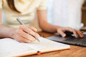 Close-up of a woman writing in a notebook while using a laptop, capturing a productive home office environment. photo