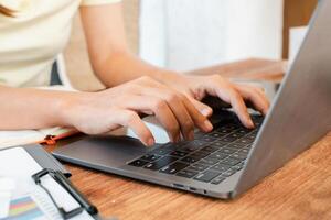 Hands typing on a laptop in a comfortable workspace, featuring a notepad and pen on a wooden desk. photo