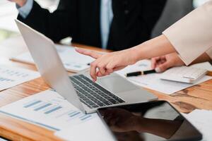 Professionals collaborating on financial analysis using a laptop, surrounded by charts and graphs in a modern office environment. photo