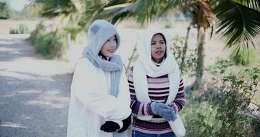 Handheld shot, Two Asian women in warm clothing stand hugging each other and chatting happily while enjoying the view in the cold morning atmosphere. video
