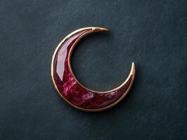 A crescent moon pendant with a gold frame and a red stone photo