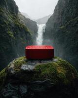 A red object sits on a mossy rock in front of a waterfall photo