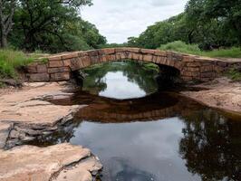 Stone bridge over a calm river surrounded by lush green trees photo
