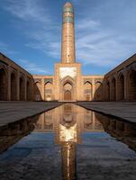 A tall minaret reflects in a puddle in a courtyard photo