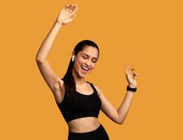 Favourite Song. Portrait Of Excited Young Sportive Lady Wearing Wireless Earbuds Listening To Music And Dancing Isolated Over Orange Studio Background. Lady With Closed Eyes Enjoying Playlist photo