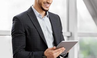 Handsome Young Arab Businessman Using Digital Tablet While Waiting At Airport Terminal, Smiling Middle Eastern Man Working Online Or Browsing Internet On Tab Computer, Enjoying Modern Technologies photo