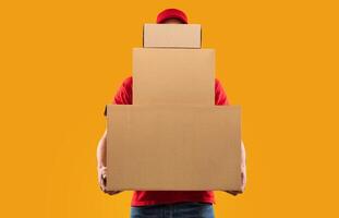 Parcels Delivery. Unrecognizable Courier Guy Holding Many Big Cardboard Boxes Delivering Packages To You Posing Standing In Studio Over Yellow Background. Postal Shipping Service Concept photo