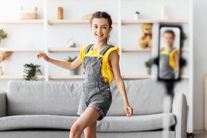 Gen Z Entertainment. Full body length of positive adolescent girl dancing filming for social network using cell phone camera, creating trendy content for likes with gadget on tripod stabilizer photo