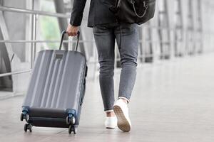 Rear View Of Unrecognizable Man Walking With Suitcase In Airport Terminal, Male Traveller Going To Flight Boarding Gate, Ready For Vacation Journey Or Business Trip, Cropped Image, Copy Space photo