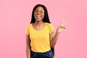 V-Sign. Successful African American Lady Gesturing Victory Symbol Smiling To Camera Standing In Studio On Blue Background, Wearing Sunglasses. Peace Gesture Concept photo