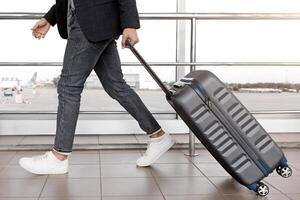 Air Transportation Concept. Unrecognizable man walking with suitcase in airport building, side view of male traveler carrying luggage, going to departure gate in terminal, cropped image, free space photo