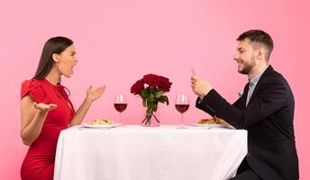 Angry Girlfriend Shouting At Indifferent Boyfriend While He Using Phone During Date Sitting At Table On Yellow Background. Studio Shot photo