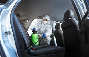 Rules of how to protect your life during coronavirus. Man in protective suit cleaning with chemicals his car, world pandemic, copy space photo