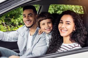 Cheerful glad millennial arab mother and father with kid go on vacation by auto and look at camera at open window. Family trip on new car, weekend together, love and relationship, positive emotions photo