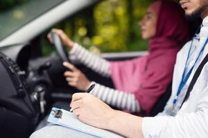 Driving School Concept. Male instructor examining muslim lady driver, holding clipboard and writing down exam results in notepad, islamic lady passing drive test, side view shot with selective focus photo