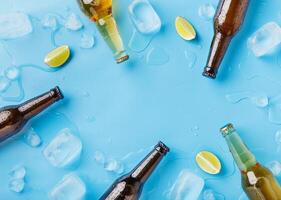 Summer party and chilled drinks. Dark and light glass beer bottles without labels with ice and pieces of lime on blue background, top view, free space photo