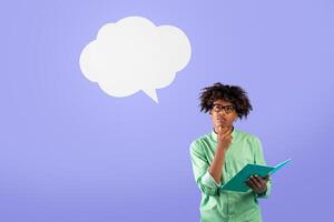 Think and make decisions. Pensive black guy in glasses holding notebook and toching chin, looking up at empty space, isolated on blue background, studio shot photo