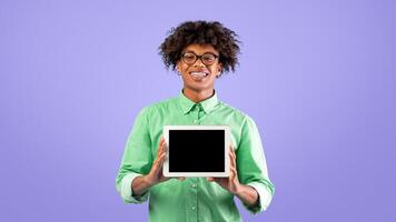 Happy african american teen guy showing new digital tablet with blank screen over blue studio background, happy teenager recommending newest mobile application for study online, copy space photo
