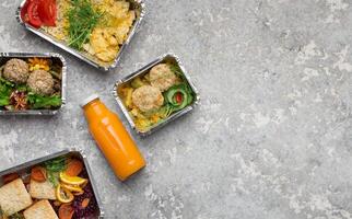 Takeout food menu, assorted healthy meals in foil containers and orange smoothie, top view, copy space photo