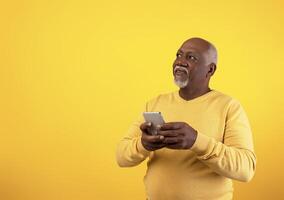 Cheerful senior African American man using mobile phone with new application, looking at empty space on orange studio background. Gadgets and mobile communication concept photo