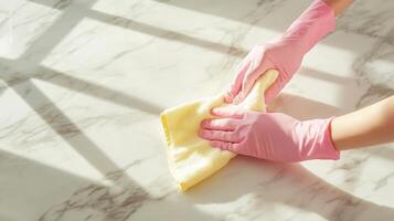 Hands wearing pink gloves carefully wipe down a marble countertop with a cloth, utilizing sunlight to enhance the tidying process during spring cleaning activities at home. photo